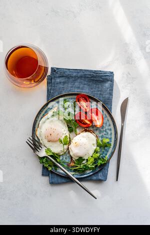 Ein köstliches und nahrhaftes Frühstück mit perfekt gebratenen Eiern, frischem Salat und Reifen Tomaten auf einer rustikalen Keramikplatte. Ideal für Starti Stockfoto