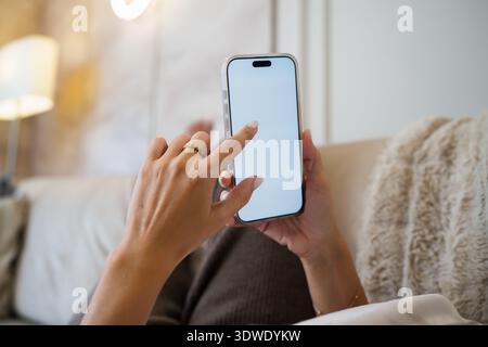 Eine Frau, die sich auf einem Sofa entspannt und ihr Smartphone mit einem leeren Bildschirm benutzt. Ihre Finger berühren sanft den Touchscreen und zeigen einen Moment der Freizeit und der technik Stockfoto