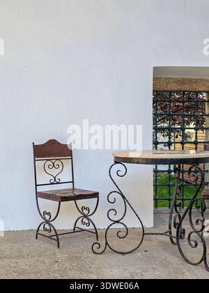 Ein schmiedeeiserner Tisch und ein Stuhl-Set mit komplizierten Scrollarbeiten verleihen jedem Innen- und Außenbereich Eleganz. Die rustikale Oberfläche unterstreicht die cl Stockfoto