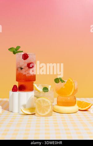 Drei Cocktails mit Himbeeren, Zitronen und Orangen mit Minzgarnitur werden auf einem Tisch mit einer weiß-gelb karierten Tischdecke Agave serviert Stockfoto