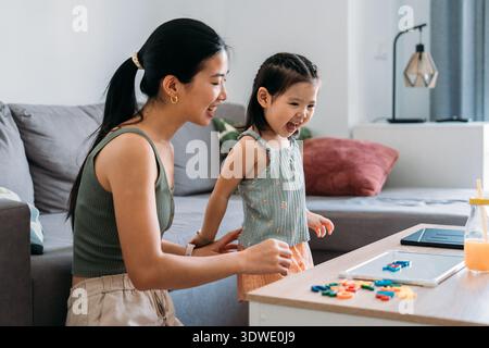 Mutter und Tochter nehmen an einem Tisch in ihrem Wohnzimmer unterhaltsame, lehrreiche Aktivitäten wahr, fördern Kreativität und lernen in einer komfortablen Familie Stockfoto