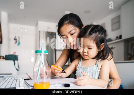 Mutter und Tochter arbeiten zu Hause kreativ. Die Mutter hilft ihrer Tochter beim Färben in einer hellen, modernen Kücheneinrichtung, Highlighti Stockfoto