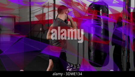Trainingsmann mit grauem T-Shirt, das schwere Boxsäcke im Fitnessstudio schützt, mit Schuhen und lila Streifen Stockfoto