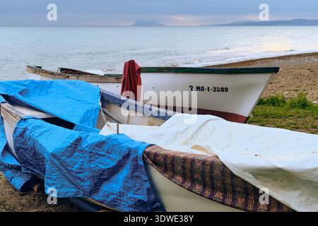 Estepona, Spanien - 02. Januar 2026: Blick auf die Fischerboote, die am Ufer ruhen, deren lebhafte Farbtöne im Kontrast zum ruhigen Meer und dem fernen Si stehen Stockfoto