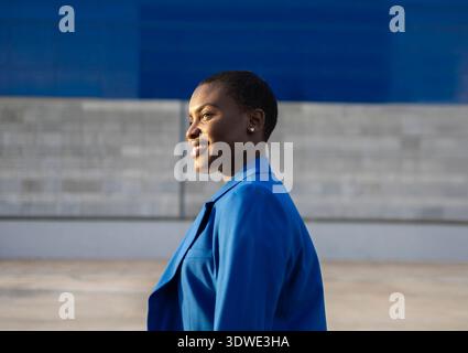 Eine selbstbewusste afrikanische Geschäftsfrau, die einen stilvollen blauen Anzug trägt, steht vor einem modernen urbanen Hintergrund und strahlt Professionalität und Führung aus Stockfoto