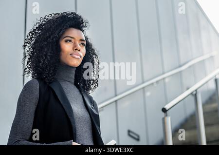 Eine selbstbewusste junge Frau steht für moderne Architektur und verkörpert einen modernen und stilvollen urbanen Lebensstil. Sie strahlt Sicherheit und Modernität aus in a c Stockfoto