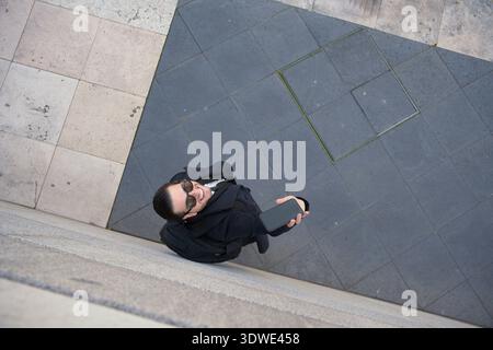 Ein Geschäftsmann im Anzug, der ein Smartphone hält und im Freien lächelt. Er kommuniziert effektiv über sein Telefon und zeigt moderne Arbeitsabläufe Stockfoto