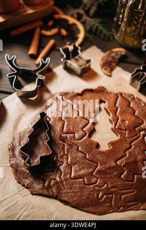 Festliche Lebkuchenkekse im Gange, mit Teig- und Keksschneidern auf Pergamentpapier, umgeben von duftenden Zimtstäbchen und getrockneten Orangen-slic Stockfoto