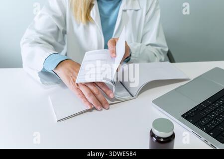 Die beschnittene, nicht erkennbare Ärztin schreibt Rezepte auf einem Schreibtisch neben einem Laptop und einer pharmazeutischen Flasche und zeigt eine Mischung aus Gesundheitswesen und Te Stockfoto