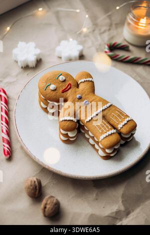 Ein bezaubernder Lebkuchenmann-Kuchen sitzt auf einem weißen Teller, umgeben von Weihnachtsdekorationen. Die Süße und Wärme der festlichen Saison i einfangen Stockfoto