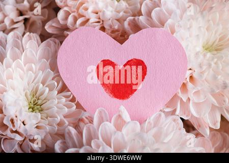 Ein rosafarbenes Papierherz mit rotem Fingerabdruckherz liegt auf einem Bett aus zarten weißen Blumen. Dieses Bild fängt das Wesen des Valentinstages ein, SYM Stockfoto