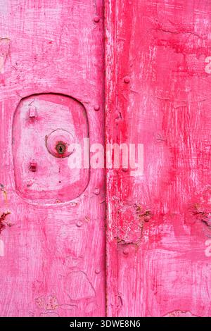 Dieses Bild zeigt eine verwitterte pinkfarbene Tür in Taiwan, Asien, die ihre rustikale Textur und veraltete Details hervorhebt. In der Nahansicht werden Roststellen und angezeigt Stockfoto