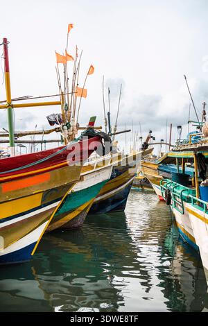 Eine lebhafte Sammlung traditioneller Fischerboote legt am belebten Hafen von Colombo an. Die leuchtenden Farben und die komplizierten Details der Boote heben sich von anderen ab Stockfoto