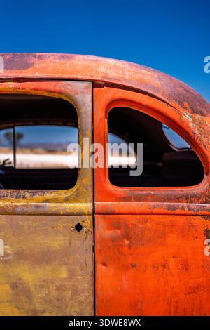 Eine detaillierte Nahaufnahme einer rustikalen Oldtimertür mit verwitterter orange-gelber Farbe unter einem klaren blauen Himmel. Die abgenutzte Struktur erfasst ein Stockfoto