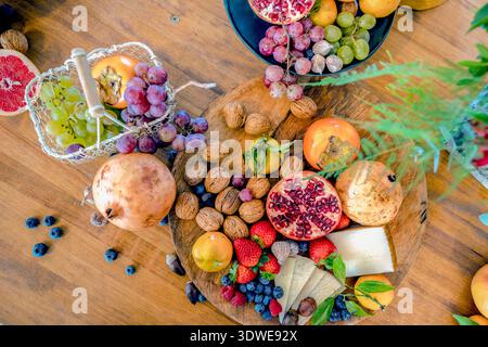Ein lebhaftes Sortiment an Früchten und Nüssen, darunter Erdbeeren, Heidelbeeren, Trauben, Käsescheiben, Mandarinen, Granatäpfel, Feigen, Persimmonen, Angebot Stockfoto