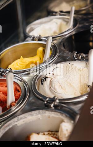 Nahaufnahme verschiedener Eisaromen, die in Edelstahlbehältern in einer Gelateria gezeigt werden. Mit leuchtenden Gelb- und Rottönen, jeweils mit einem Dedi Stockfoto