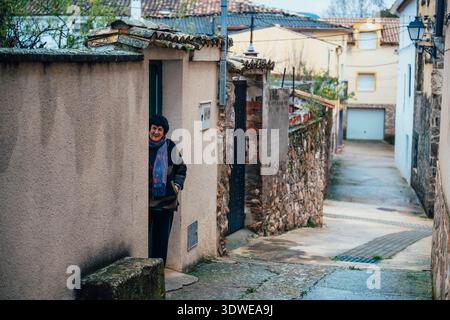 Eine Frau steht in einer Tür einer rustikalen Dorfstraße in Salmeron, Guadalajara, und fängt mit Steinmauern und traditionellem Ar das Wesen des ländlichen Lebens ein Stockfoto