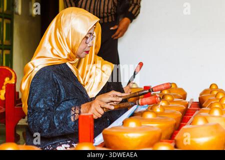 Eine Frau in goldenem Hijab und traditioneller Kleidung spielt das Gamelan, ein traditionelles javanisches Musikinstrument, das sich intensiv auf die Gestaltung von M konzentriert Stockfoto