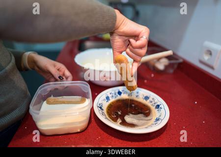 Eine Person bereitet hausgemachtes Tiramisu zu, indem sie Marienfinger in Kaffee taucht und den Prozess der Zubereitung dieses klassischen italienischen Desserts in einer Hausküche zeigt Stockfoto