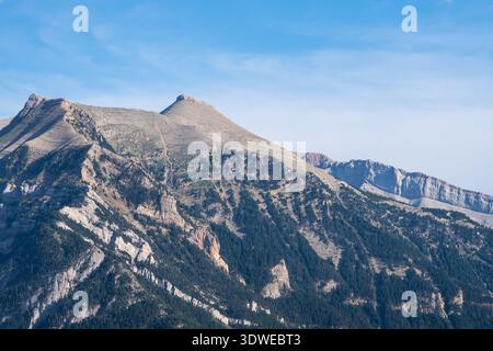 Ein atemberaubender Blick auf zerklüftete Berggipfel, bedeckt mit Waldstücken und felsigen Ausbissen, vor einem klaren blauen Himmel in den französischen Pyrenäen. Stockfoto