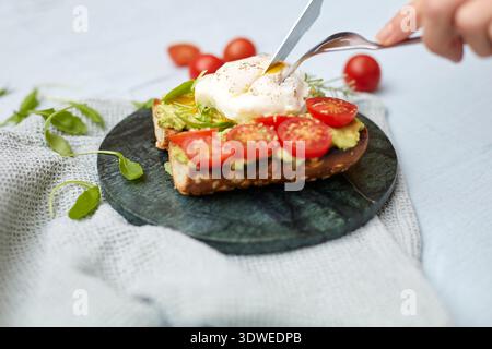Gesundes Frühstück mit einem köstlichen offenen Sandwich mit Avocado, Tomatenscheiben und einem perfekten pochierten Ei, alles auf Vollkornbrot Stockfoto