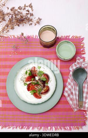 Ein lebendiger Salat mit frischen Tomaten auf cremigem Naturjoghurt, garniert mit Petersilie, Quinoa und Chiasamen. Eine perfekte Mischung aus knusprigen, cremigen, Stockfoto