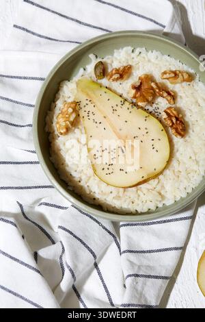 Eine köstliche Schüssel mit cremigem Reis aus pflanzlicher Milch, garniert mit frischen Birnenscheiben, knusprigen Walnüssen, Chiasamen und einem Honig für einen swe Stockfoto