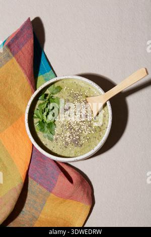 Ein leuchtend grüner Smoothie in einer Keramikschale mit frischer Petersilie und bestreuten Samen. Ein Holzlöffel liegt in der Schüssel, neben einem bunten Tuch n Stockfoto