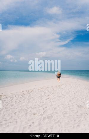Ein einsamer Mann spaziert entlang des unberührten weißen Sandes eines tropischen Strandes auf den Philippinen, umgeben von ruhigem türkisfarbenem Wasser und teilweise bewölktem Himmel. Stockfoto