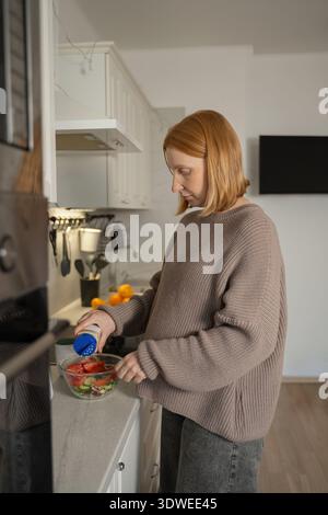 Schwangere Frau in einer gemütlichen Hausküche, sorgfältig einen frischen Salat mit Gemüse und Gemüse zubereiten, betont einen gesunden Lebensstil während der Schwangerschaft. Stockfoto