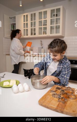 Mutter und Tochter genießen die gute Zeit beim Backen in ihrer Küche. Die Tochter mischt Zutaten in einer Schüssel, während die Mutter andere b zubereitet Stockfoto
