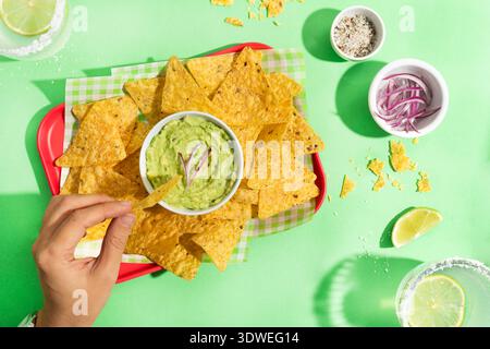 Leckere mexikanische Nachos serviert mit cremiger Guacamole auf einem hellen, farbenfrohen Hintergrund. Die knusprigen Chips und der glatte Dip sorgen für einen einladenden Snack, perfekt Stockfoto