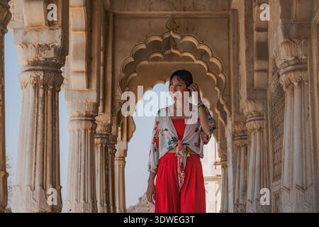 Eine Frau in leuchtend roter Kleidung bewundert die komplizierten Steinschnitzereien eines historischen indischen Tempels und genießt die ruhige und spirituelle Atmosphäre des Stockfoto