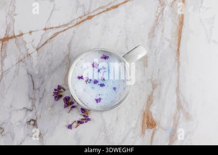 Ein beruhigender blauer Matcha Latte mit zarten violetten Blütenblättern sitzt elegant auf einer Marmoroberfläche und schafft eine perfekte Mischung aus Ruhe Stockfoto