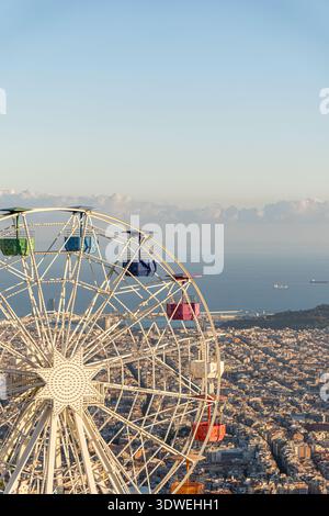 Ein atemberaubender Panoramablick von Tibidabo aus mit einem farbenfrohen Riesenrad vor der Kulisse eines weitläufigen Barcelona, umgeben von warmen Sonnen Stockfoto