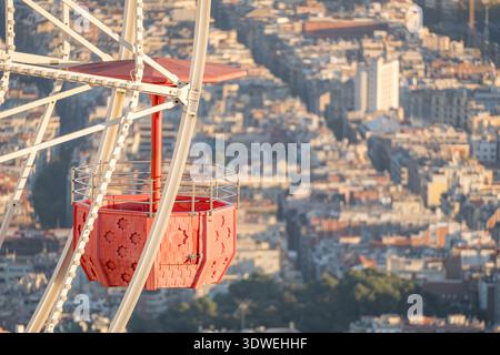 Eine hellrote Riesenradkabine in Tibidabo bietet einen atemberaubenden Blick auf Barcelonas weitläufige Stadtlandschaft während des Sonnenuntergangs und strahlt ein warmes Leuchten über dem Stockfoto