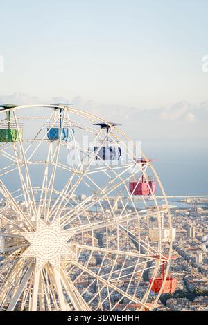Ein pulsierendes Riesenrad dominiert den Blick auf Barcelona von Tibidabo aus bei einem atemberaubenden Sonnenuntergang. Helle Farben bilden einen malerischen Kontrast zum Stockfoto