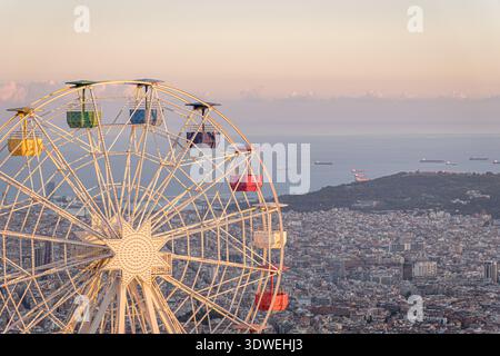 Ein atemberaubender Blick von Tibidabo aus fängt ein farbenfrohes Riesenrad mit Blick auf Barcelona bei Sonnenuntergang ein, während die Stadtlandschaft und das Mittelmeer einen br Stockfoto