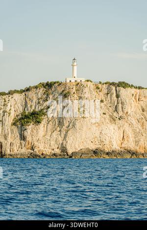 Ein malerischer Leuchtturm auf einer zerklüfteten Klippe in Griechenland mit Blick auf das tiefblaue Meer. Die Szene fängt die Gelassenheit und zeitlose Schönheit von Th ein Stockfoto