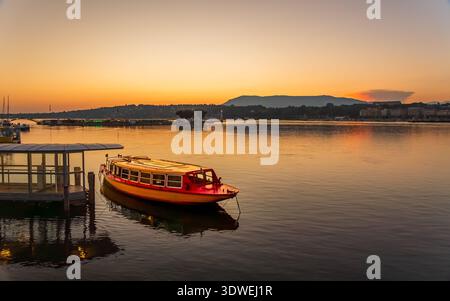 Eine ruhige Morgenszene in Genf während der goldenen Stunde zeigt einen ruhigen Blick auf ein Boot, das vom ruhigen, reflektierenden Wasser angedockt ist, und schafft Bilder Stockfoto