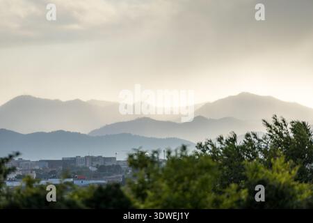 Malerischer Blick auf Castellon de la Plana mit einer Stadtlandschaft mit Gebäuden und einer Kulisse von sonnendurchfluteten Bergen unter einem bewölkten Himmel, umgeben von üppigem Grün Stockfoto