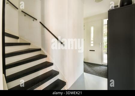 Ein elegantes und modernes Interieur mit einer Treppe mit schwarzen Stufen und minimalistischem Design. Die hellen Farben verstärken die Eleganz und Einfachheit des Stockfoto