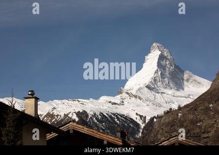 Das berühmte Matterhorn erhebt sich majestätisch mit einem klaren blauen Himmel und überblickt die rustikalen Dächer von Zermatt im Wallis, Schweiz, und schafft ein perfektes Ambiente Stockfoto
