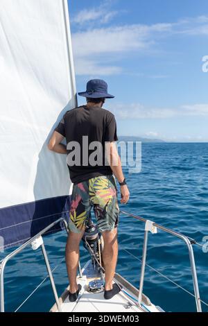 Ein Mann steht auf einem Segelboot und blickt über das riesige Mittelmeer unter einem klaren blauen Himmel. Die ruhige Szene fängt das Wesen der Ozeanforschung ein Stockfoto