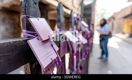 Lila Gebetstafeln hängen an einem Holzzaun im Cheng Huang Tempel in der antiken Stadt Pingyao, China. Eine Frau in blauer Jeans fotografiert das heilige Settin Stockfoto