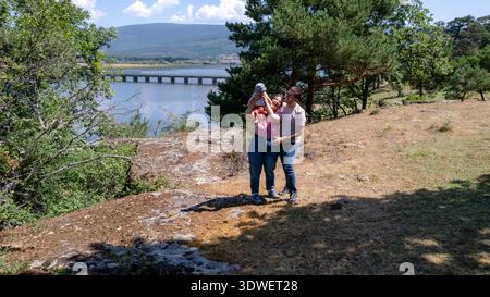 Eine fröhliche Familie verbringt schöne Zeit zusammen an einem malerischen See in Vinuesa, Soria, Spanien. Die Eltern halten liebevoll ihr Baby, umgeben von nat Stockfoto