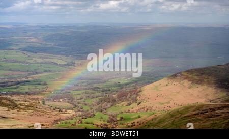Ein lebhafter Regenbogenbogen zieht sich über die üppig grünen Hügel und Täler des Brecon Beacons National Park. Diese atemberaubende Landschaft fängt die ruhige Schönheit von ein Stockfoto