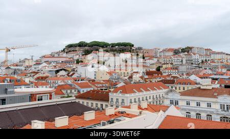 Panoramablick auf Lissabons bezaubernde Gebäude mit rotem Dach und Schloss Sao Jorge, eingebettet in das üppige Grün des Hintergrunds, und fängt den Höhepunkt der Stadt ein Stockfoto
