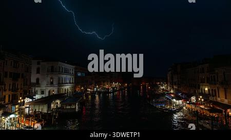 Dramatische Blitze erleuchten den Nachthimmel über dem Canal Grande von Venedig aus gesehen von der Rialto-Brücke. Das beleuchtete Stadtbild spiegelt sich in der Büste Stockfoto