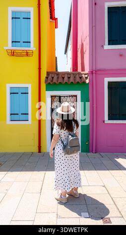 Ein Reisender mit Hut und Rucksack erkundet die lebhaften, farbenfrohen Häuser von Burano, Venedig, Italien. Die malerische Straße ist in Sonnenlicht getaucht Stockfoto
